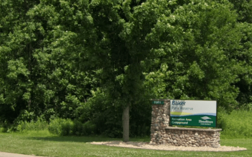 Sign for Baker Park Reserve, featuring a stone base and surrounded by lush green trees and grass.