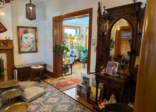 Cozy interior with plants, artwork, and decorative furniture, featuring a mirror and a patterned rug.