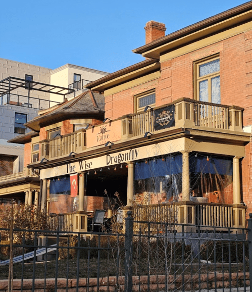 A charming brick building with a porch, featuring a sign for "The Wise Dragonfly" café.