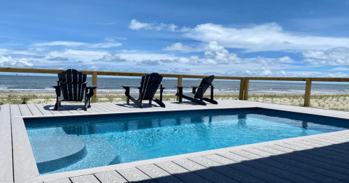 A serene poolside view with three black chairs overlooking the ocean and a clear blue sky.