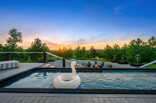 A serene pool with a swan float, overlooking a sunset and surrounded by trees and outdoor seating.