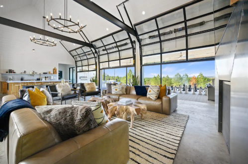 Spacious modern living room with large windows, cozy seating, and a view of nature outside.
