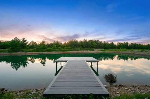 A serene dock extends into a calm lake, surrounded by lush greenery and a colorful sunset sky.