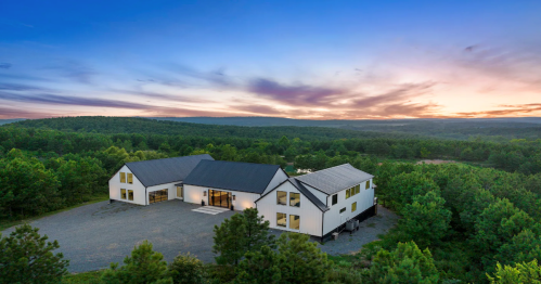 A modern white house surrounded by trees, set against a colorful sunset sky.