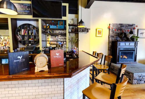 A cozy bar area with a fireplace, wooden stools, and menus displayed on the counter. Warm, inviting atmosphere.