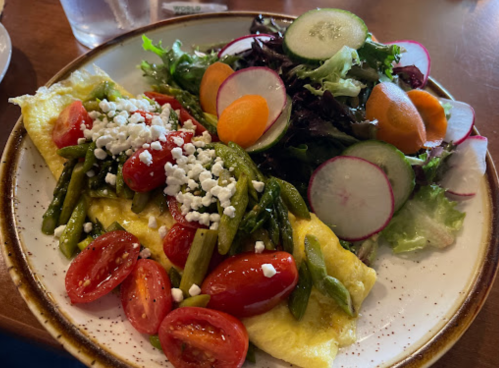 A plate with an omelette topped with tomatoes and asparagus, alongside a fresh salad with mixed greens and radishes.
