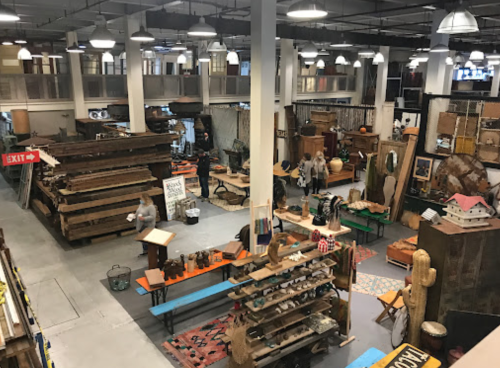 A spacious vintage market filled with wooden furniture, decor items, and shoppers exploring the eclectic displays.