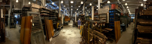 A panoramic view of a large warehouse filled with shelves of materials and tools, with people walking through the aisles.