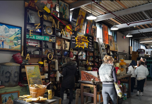 A bustling antique shop filled with colorful artwork, vintage items, and shoppers exploring the eclectic displays.