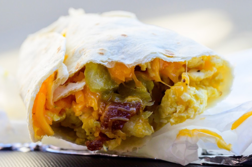 Close-up of a breakfast burrito filled with scrambled eggs, cheese, and green peppers wrapped in a flour tortilla.