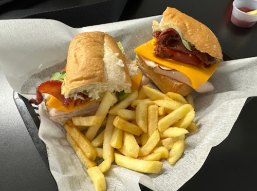 Two sandwiches with bacon, cheese, and lettuce, served with a side of golden French fries in a basket.