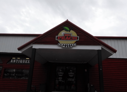 Sign for "Big Peach Antiques Mall" on a red wooden building under a cloudy sky.