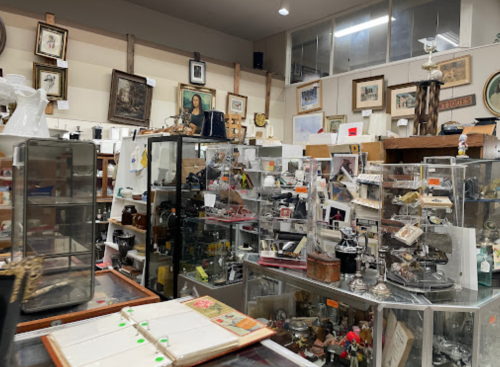 A cluttered antique shop filled with various collectibles, glass display cases, and vintage items on shelves.