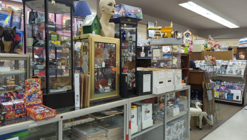 A cluttered antique shop filled with display cases, collectibles, toys, and various vintage items.