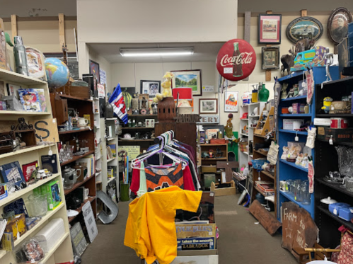 A cluttered antique shop filled with various items, including clothing, collectibles, and vintage decor on shelves.