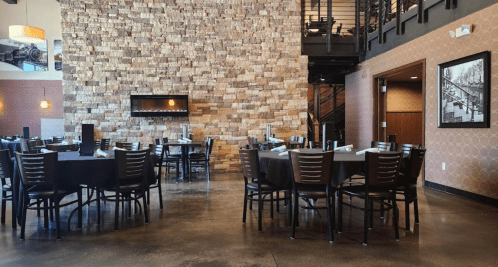 Interior of a restaurant featuring a stone wall, tables with black tablecloths, and a warm, inviting atmosphere.