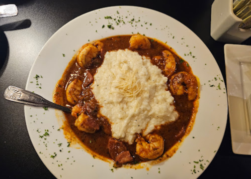 A plate of shrimp in a rich sauce served over creamy grits, garnished with herbs and a sprinkle of cheese.