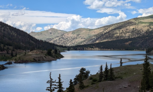 A serene lake surrounded by mountains and trees under a partly cloudy sky.