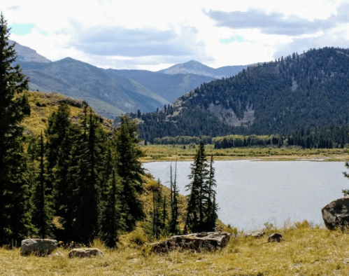 A serene landscape featuring a lake surrounded by mountains and lush greenery under a partly cloudy sky.