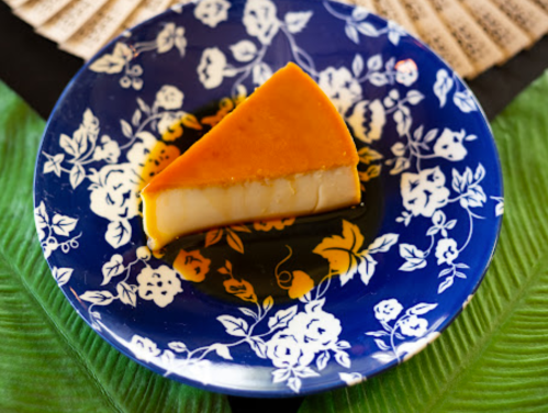 A slice of flan on a blue floral plate, resting on a green leaf background.