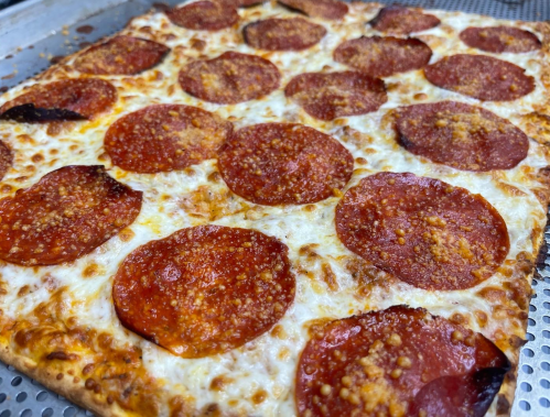 A close-up of a square pizza topped with melted cheese and pepperoni slices, baked to a golden brown.
