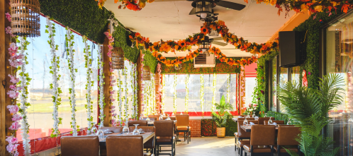 Brightly decorated restaurant interior with floral arrangements, greenery, and wooden tables set for dining.