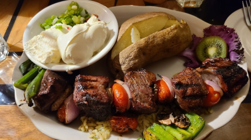 A plate featuring skewered grilled meat, vegetables, a baked potato, salad, and a scoop of ice cream.