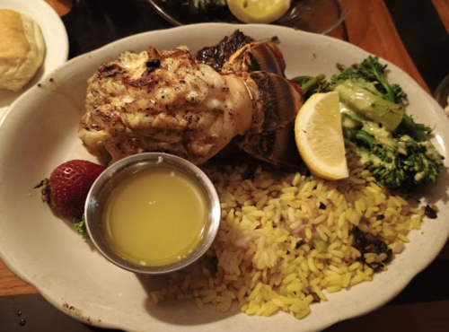 A plate of grilled lobster tail, rice, broccoli, a lemon wedge, and a small cup of melted butter, with a strawberry.