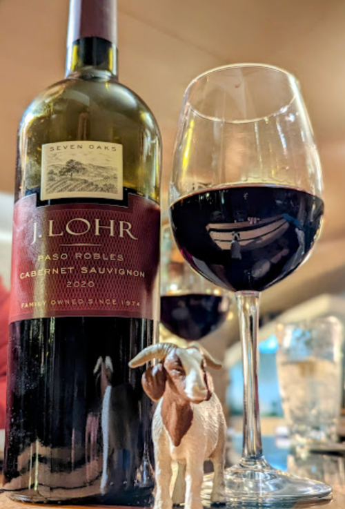 A bottle of J. Lohr Cabernet Sauvignon, a glass of red wine, and a small goat figurine on a table.