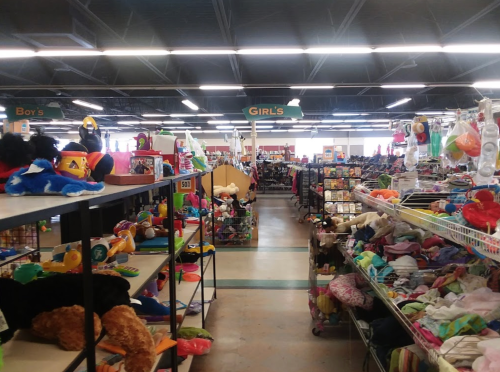 A brightly lit store aisle filled with shelves of toys and clothing, labeled for boys and girls.