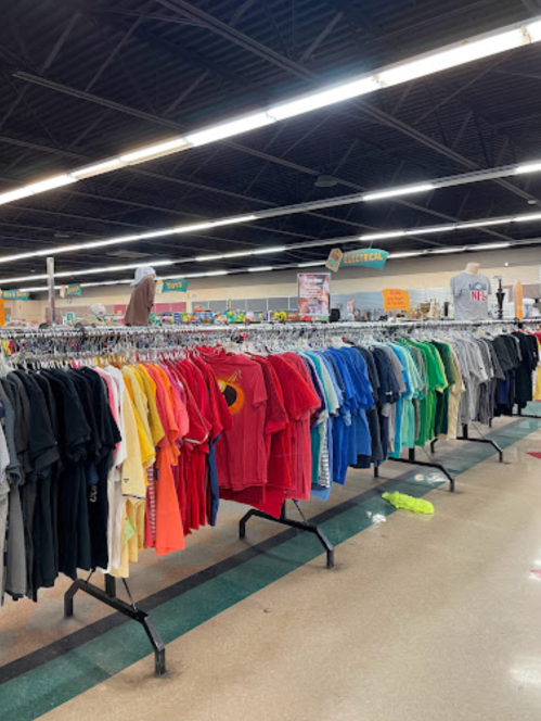 A clothing rack filled with colorful t-shirts in a spacious store, with mannequins and signs in the background.