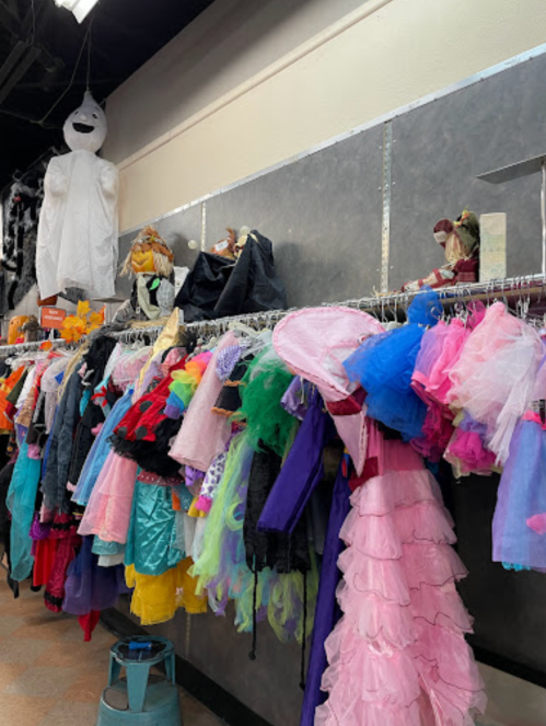 A colorful display of costumes hanging on racks, with a ghost costume and various accessories in the background.