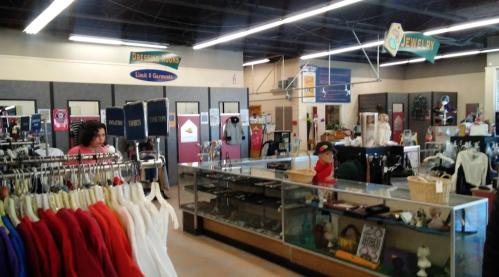 A spacious thrift store interior with clothing racks, display cases, and various merchandise on shelves.