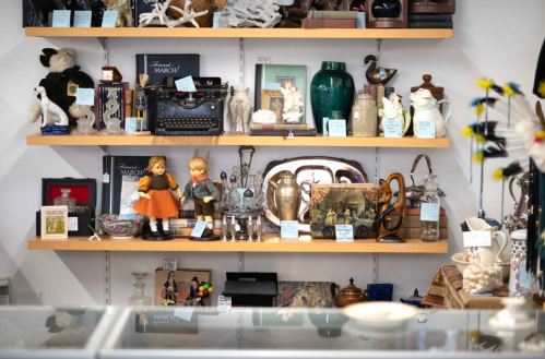 A display of vintage items, including dolls, typewriters, and various collectibles on wooden shelves.