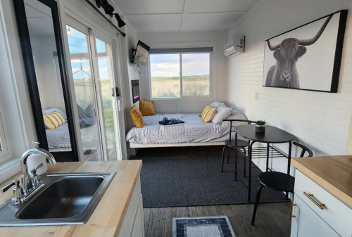 Cozy interior of a tiny home featuring a kitchen, dining table, and a bed with decorative pillows.