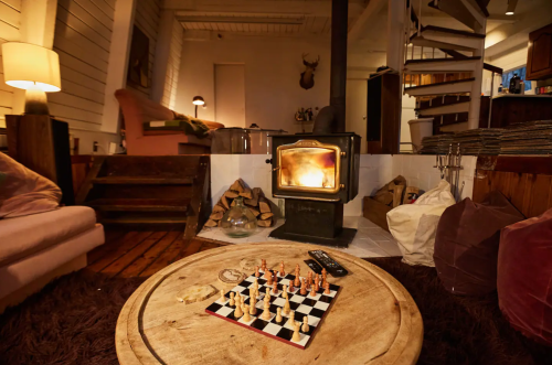 Cozy living room with a chessboard on a wooden table, a warm fireplace, and soft seating in a rustic setting.