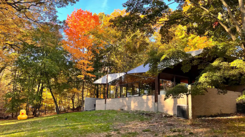 A modern building surrounded by vibrant autumn foliage, featuring colorful trees and a clear blue sky.