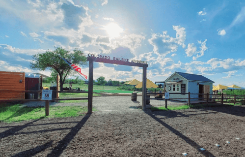 Entrance to Colorado Railbike Warehouse with a blue sky, clouds, and a grassy field in the background.