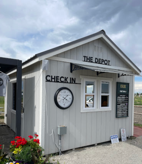 A small, white building labeled "The Depot" with a clock, check-in window, and flowers in front.