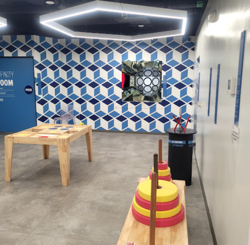 A modern room with geometric blue wall patterns, a wooden table, colorful stacking rings, and a display screen.