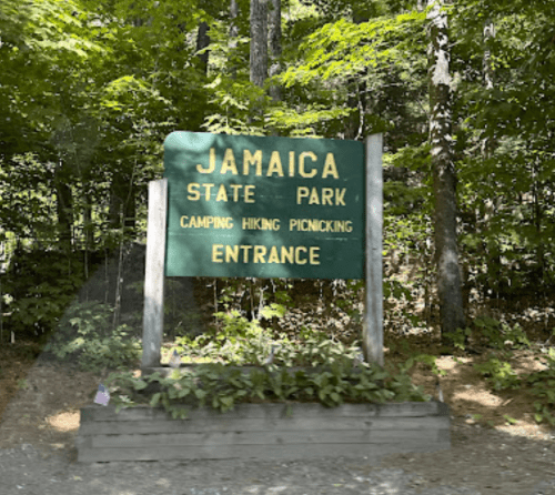 Sign for Jamaica State Park, indicating entrance for camping, hiking, and picnicking, surrounded by trees.