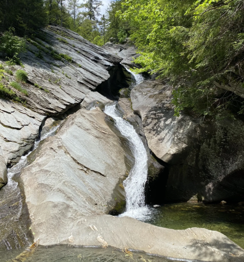 A serene waterfall cascading over smooth, rocky terrain surrounded by lush greenery and trees.
