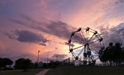 A ferris wheel silhouetted against a colorful sunset sky with clouds.