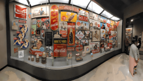 A display case filled with vintage Coca-Cola advertisements and memorabilia, showcasing various promotional items and designs.