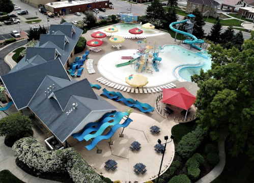 Aerial view of a vibrant water park with slides, pools, umbrellas, and lounge chairs surrounded by greenery.