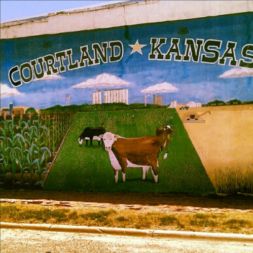 Mural depicting rural life in Courtland, Kansas, featuring cornfields, cows, and farm equipment under a blue sky.