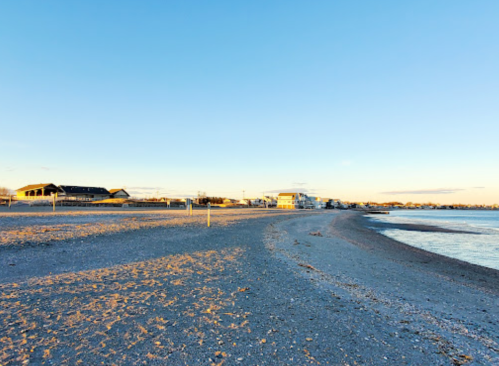 A serene beach at sunset, with gentle waves lapping at the shore and buildings in the distance.