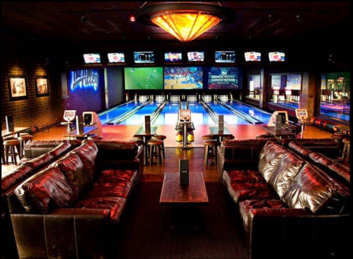 A stylish bowling alley with leather seating, a large screen, and multiple lanes illuminated in a vibrant setting.