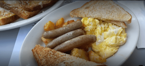 A plate of scrambled eggs, sausage links, hash browns, and toasted bread.