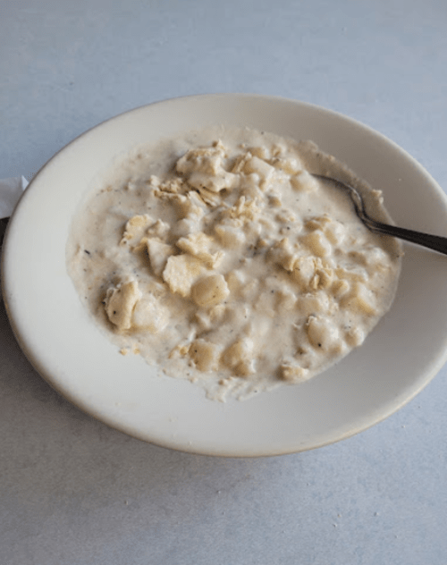 A bowl of creamy chicken and dumplings with a spoon resting inside.